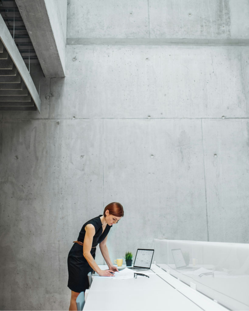 Woman in a fair-faced finish concrete space reading drawings at a desk