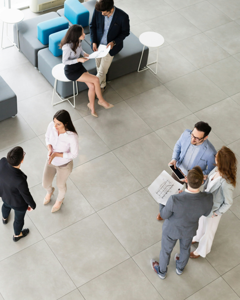 Picture from overhead of 7 people in groups of two and three talking and reading a construction drawing