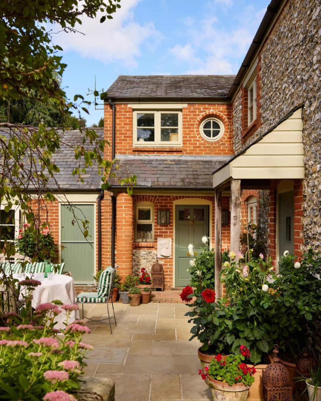 Image of a residential house with red brick facades, green front doors and flowery garden
