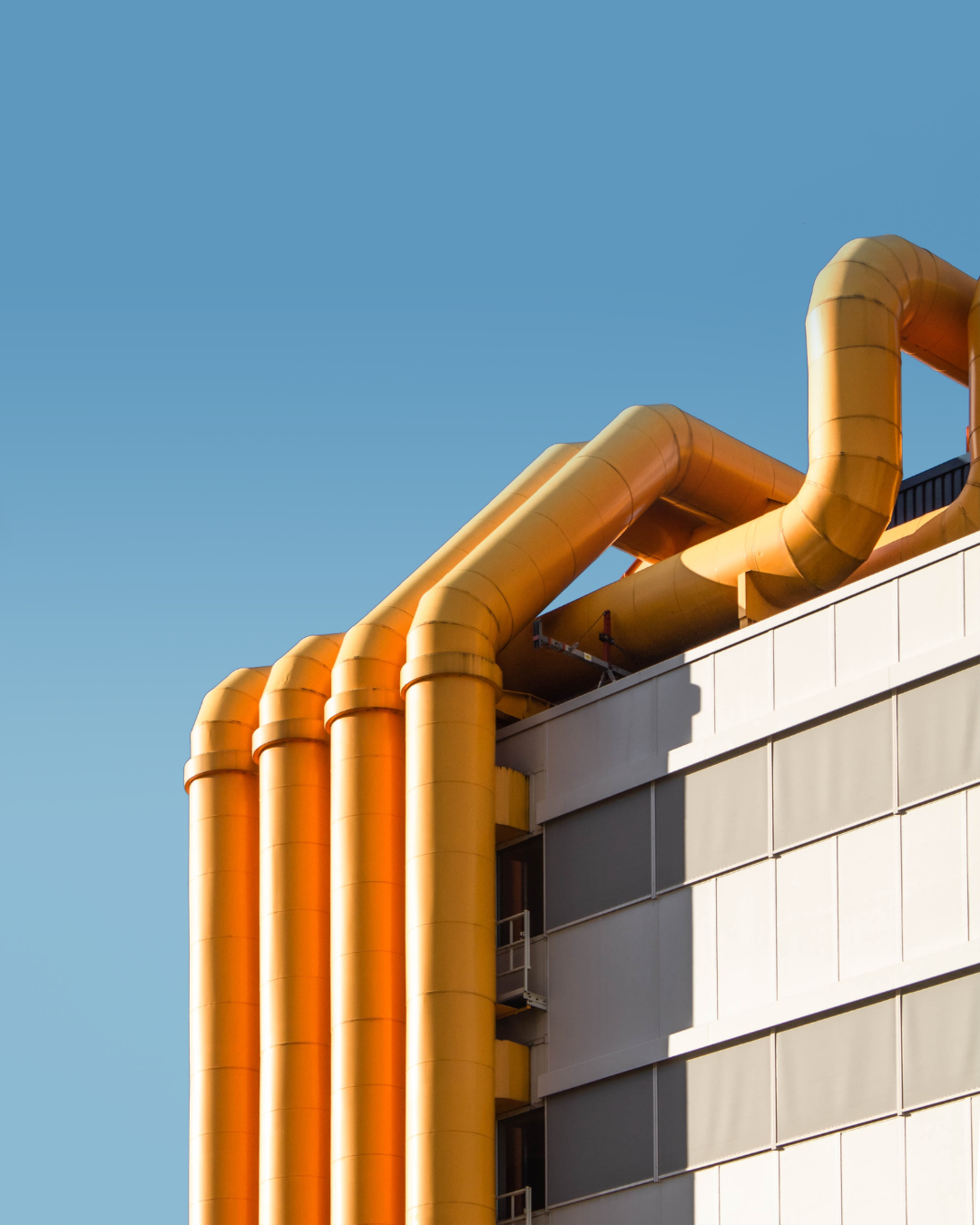 Yellow pipe and ductwork going up the side of a white building onto the roof